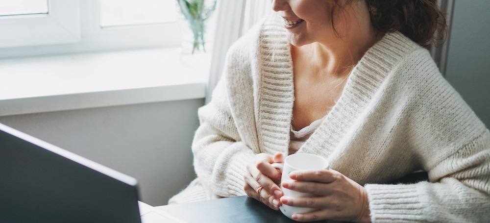 Smiling brunette woman holding cozy, warm drink during online therapy session