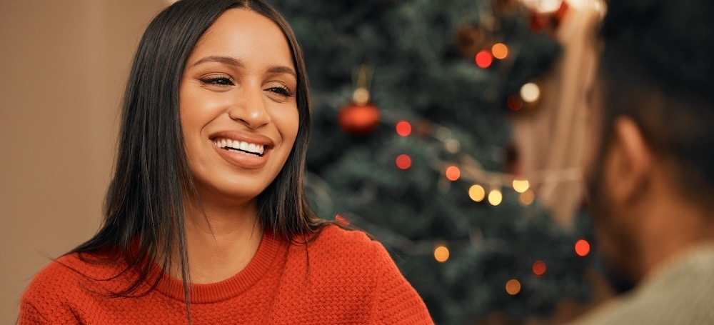 Woman having a warm drink while bonding with her partner at home in front of holiday christmas tree.