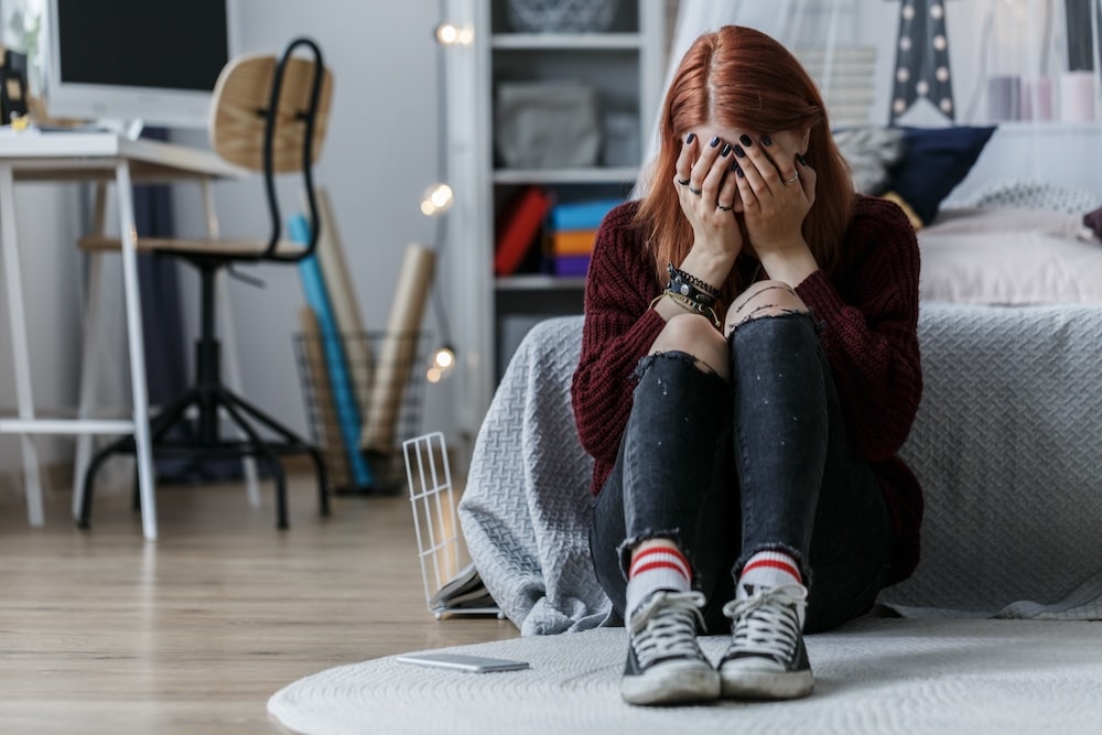 Teenage girl sitting on the floor with head in her heands