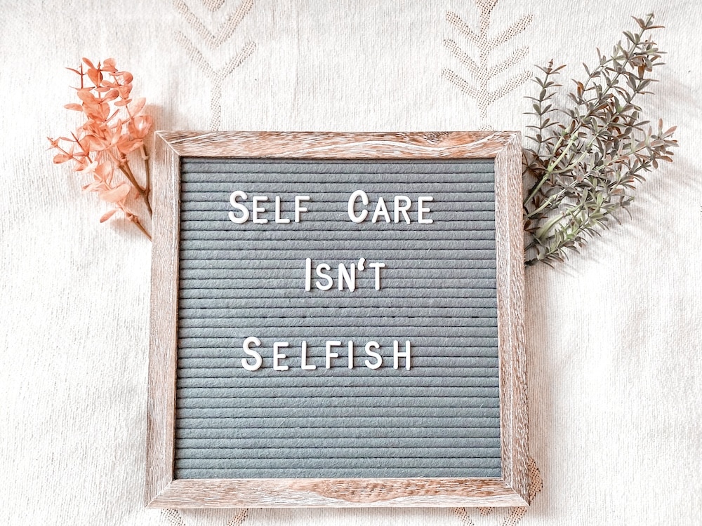 Sign that says "self-care isn't selfish" with leaves behind it