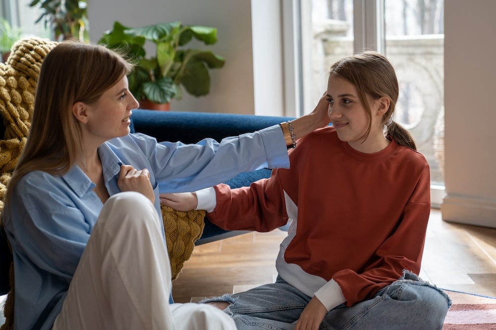 Young woman mother sitting on floor with teenage daughter having healthy, supportive conversation.